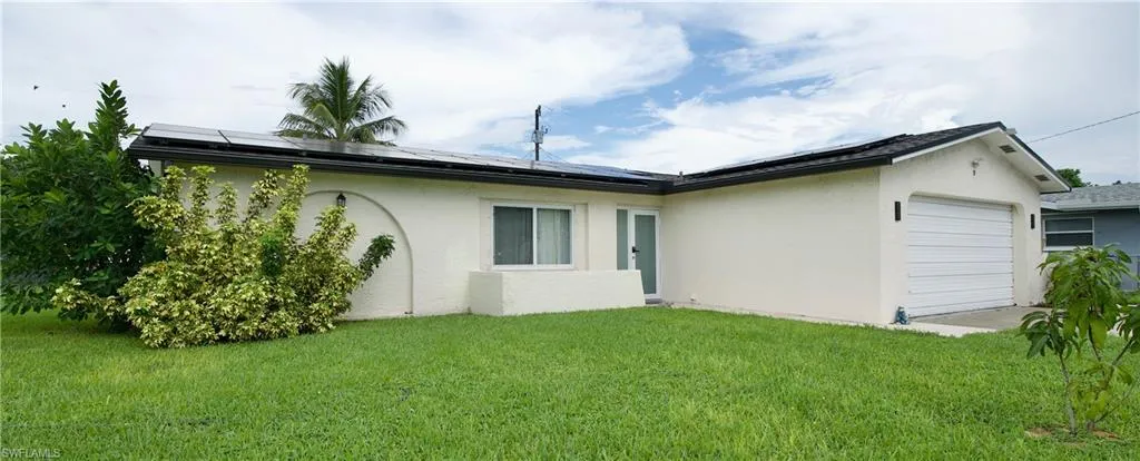 Back of property featuring roof mounted solar panels, stucco siding, a garage, and a yard
