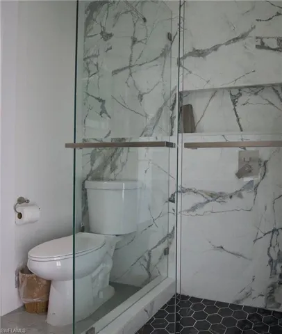 Full bath with toilet and a marble finish shower