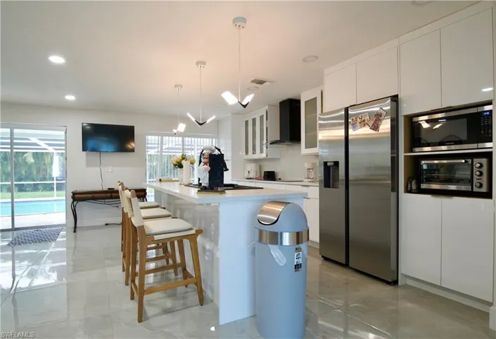 Kitchen featuring stainless steel appliances, white cabinetry, hanging light fixtures, wall chimney exhaust hood, and recessed lighting