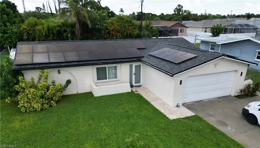 Single story home featuring roof mounted solar panels, driveway, stucco siding, a garage, and a front lawn