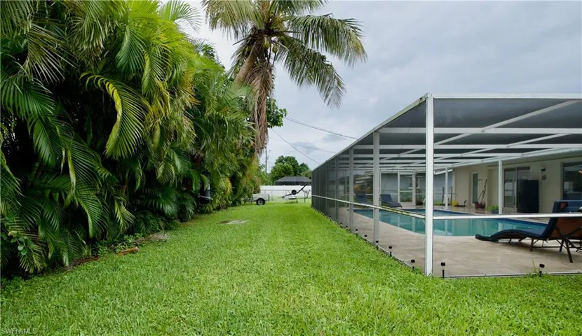 View of grassy yard with a sunroom, glass enclosure, an outdoor pool, and a patio