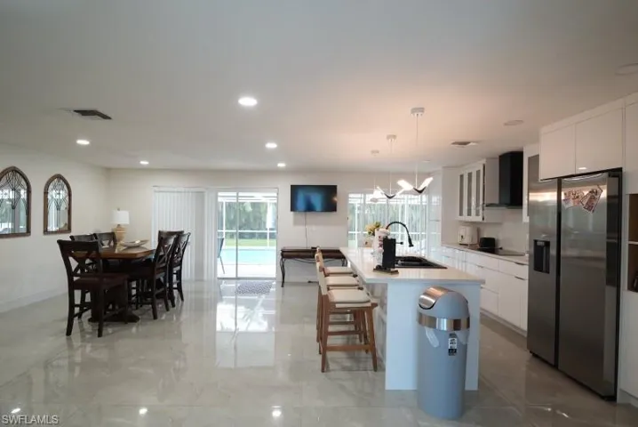 Kitchen with white cabinetry, stainless steel fridge with ice dispenser, modern cabinets, a kitchen island with sink, and recessed lighting