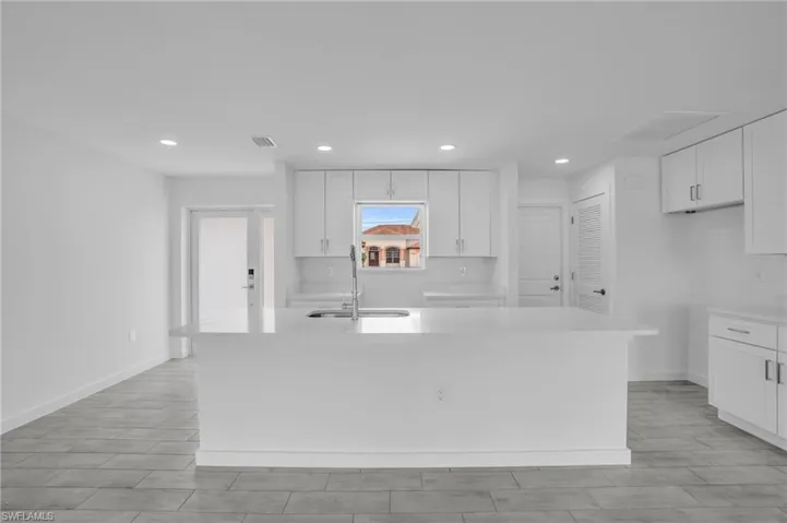 Kitchen featuring sink, white cabinets, and an island with sink