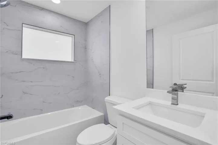 Full bathroom with vanity, tiled shower / bath combo, and toilet
