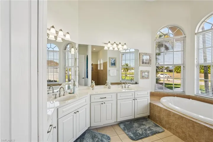 Bathroom with double vanity, light tile patterned flooring, a bath, and a high ceiling
