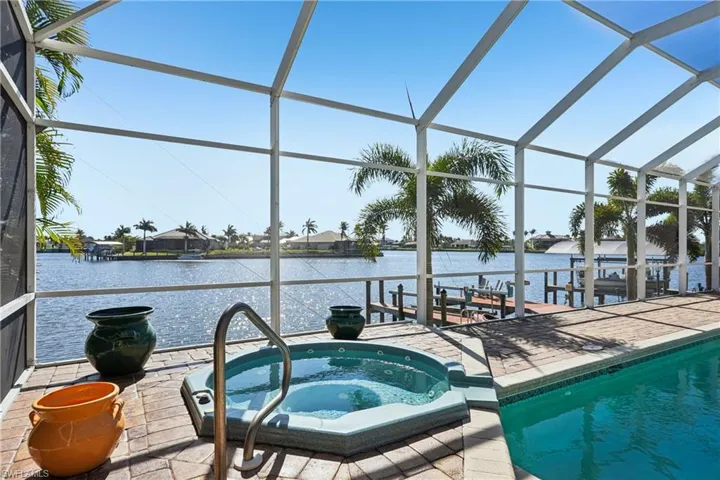 Dock featuring an in-ground hot tub, a sunroom, glass enclosure, an outdoor pool, and a water view