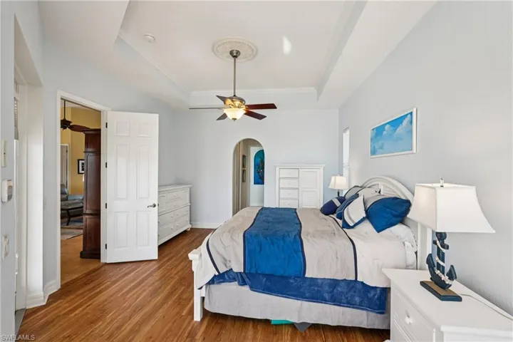 Bedroom with a tray ceiling, wood finished floors, arched walkways, and ceiling fan