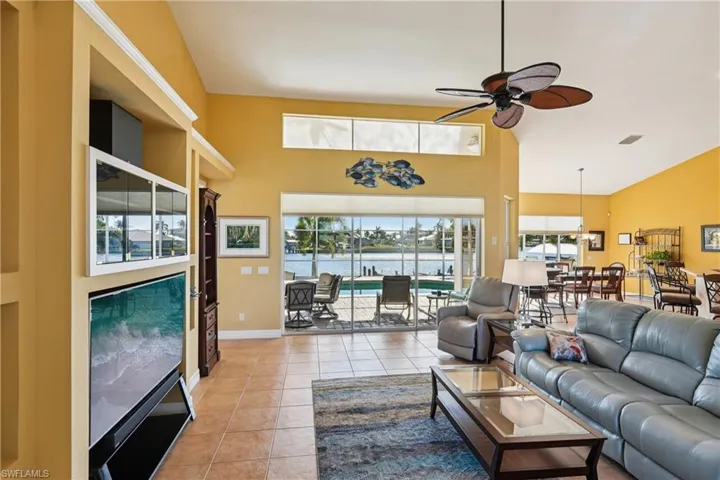 Living room with a water view, a ceiling fan, a sunroom, light tile patterned floors, and a high ceiling