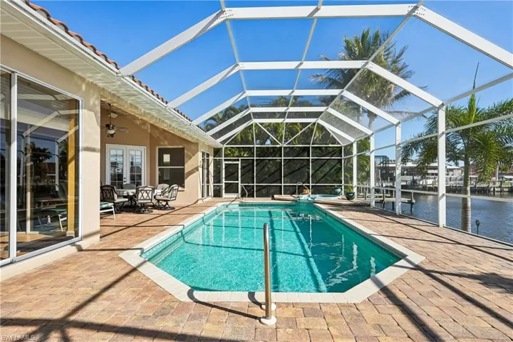 Combined pool / hot tub featuring a patio, a sunroom, glass enclosure, a water view, and french doors