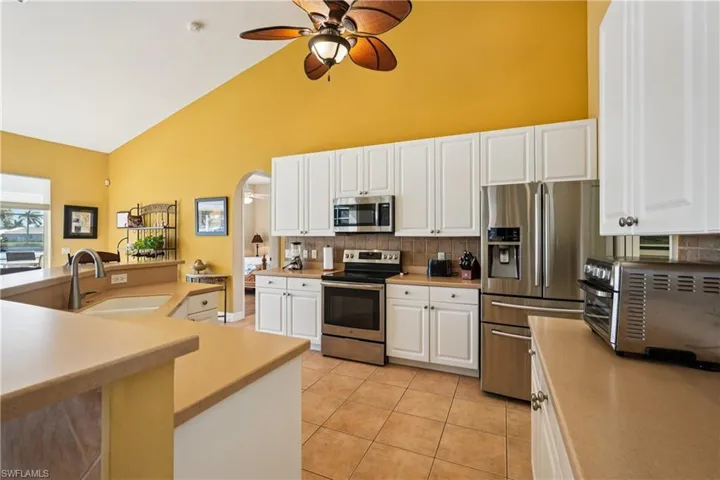 Kitchen with white cabinetry, stainless steel appliances, a ceiling fan, arched walkways, and light countertops