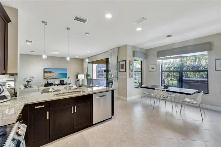 Kitchen with a wealth of natural light, dishwasher, hanging light fixtures, and light stone counters
