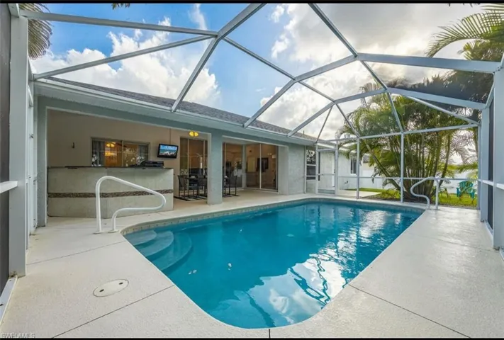 Outdoor pool featuring a sunroom, a patio, glass enclosure, and an outdoor bar