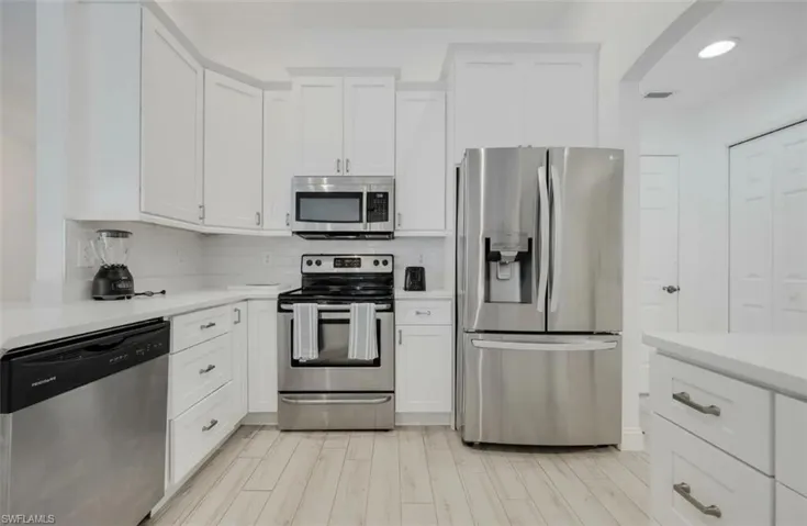 Kitchen with stainless steel appliances, white cabinetry, light wood-style flooring, arched walkways, and recessed lighting