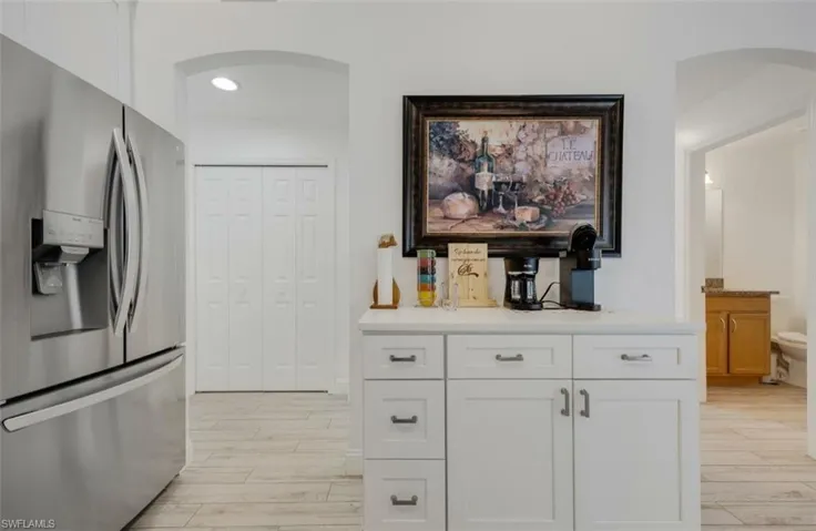 Kitchen with stainless steel fridge, arched walkways, light wood-type flooring, light countertops, and recessed lighting