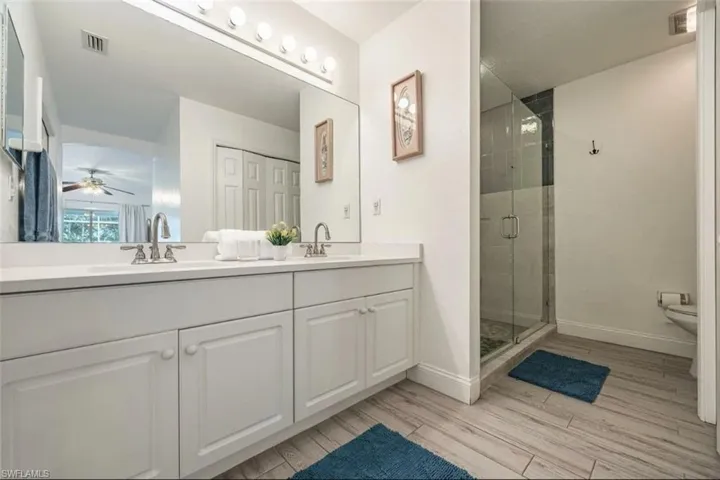 Full bathroom featuring double vanity, a stall shower, light wood-style floors, and a ceiling fan