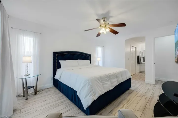 Bedroom featuring wood tiled floors, ceiling fan, multiple windows, and arched walkways