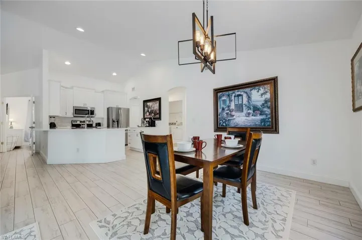 Dining room featuring arched walkways, light wood-style flooring, vaulted ceiling, and a chandelier