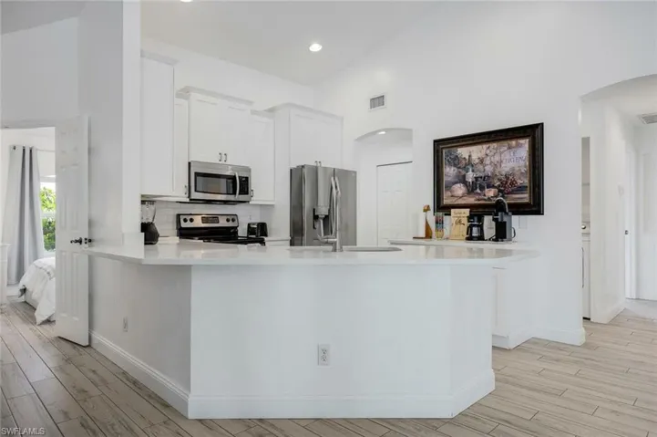 Kitchen featuring a peninsula, white cabinets, stainless steel appliances, arched walkways, and light wood-type flooring
