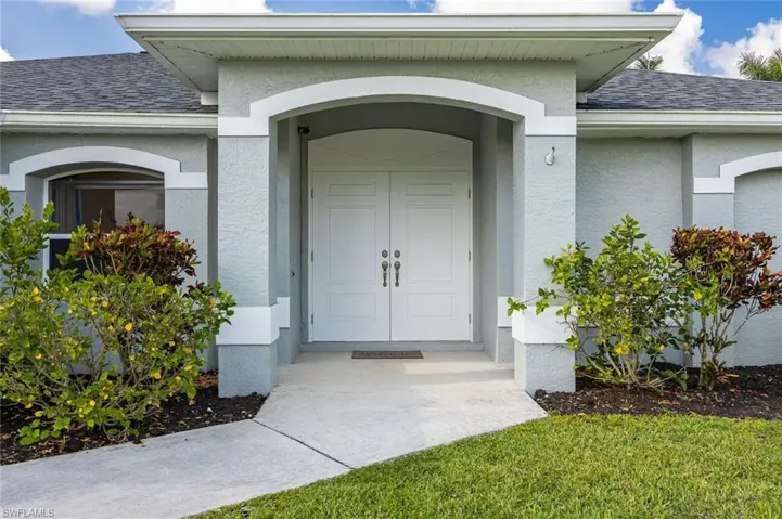 View of exterior entry featuring roof with shingles and stucco siding