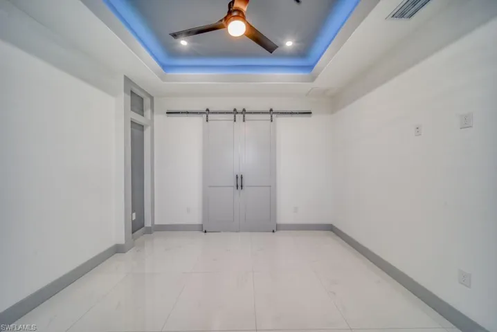 Spare room featuring a barn door, a tray ceiling, baseboards, and a ceiling fan