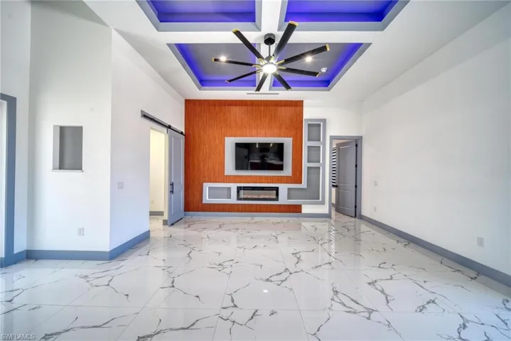 Unfurnished living room featuring baseboards, coffered ceiling, a barn door, a raised ceiling, and light marble finish flooring