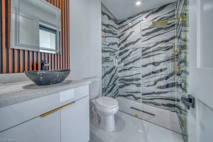 Full bath with a marble finish shower, toilet, and vanity