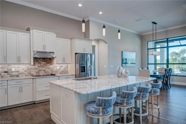 Kitchen with ornamental molding, arched walkways, white cabinets, light stone counters, and backsplash
