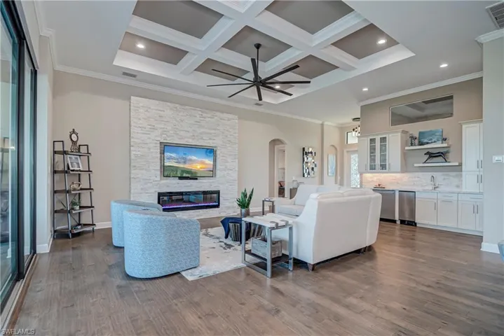 Living area featuring arched walkways, ornamental molding, a fireplace, coffered ceiling, and dark wood finished floors