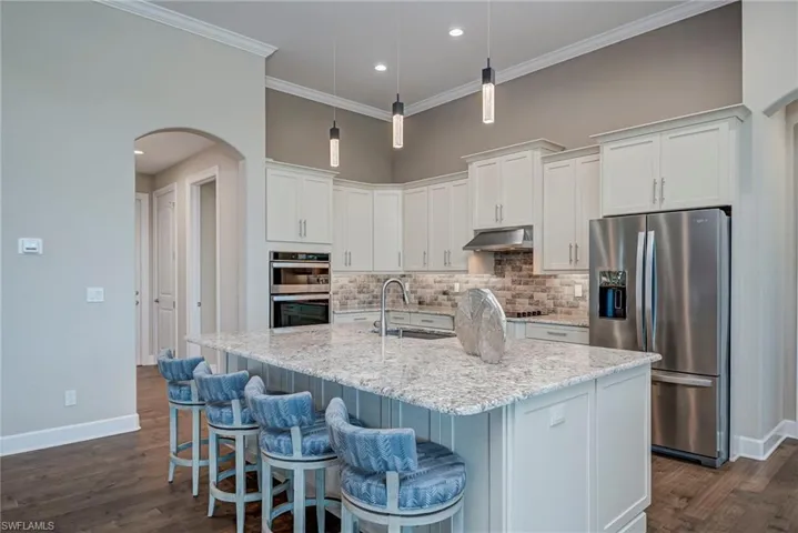 Kitchen with arched walkways, appliances with stainless steel finishes, white cabinetry, backsplash, and ornamental molding