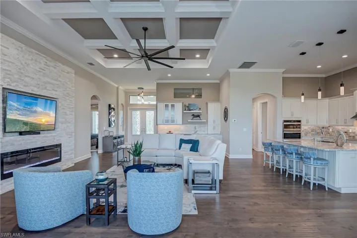 Living area with arched walkways, a stone fireplace, dark wood-style floors, a high ceiling, and ornamental molding