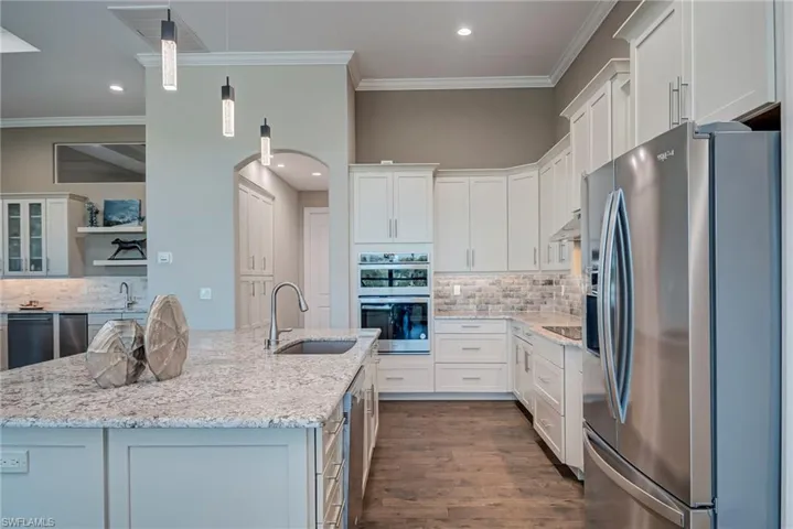 Kitchen featuring appliances with stainless steel finishes, tasteful backsplash, dark wood-type flooring, white cabinetry, and light stone countertops