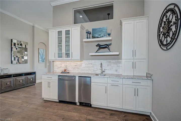 Kitchen with open shelves, white cabinets, dishwasher, light stone counters, and decorative backsplash