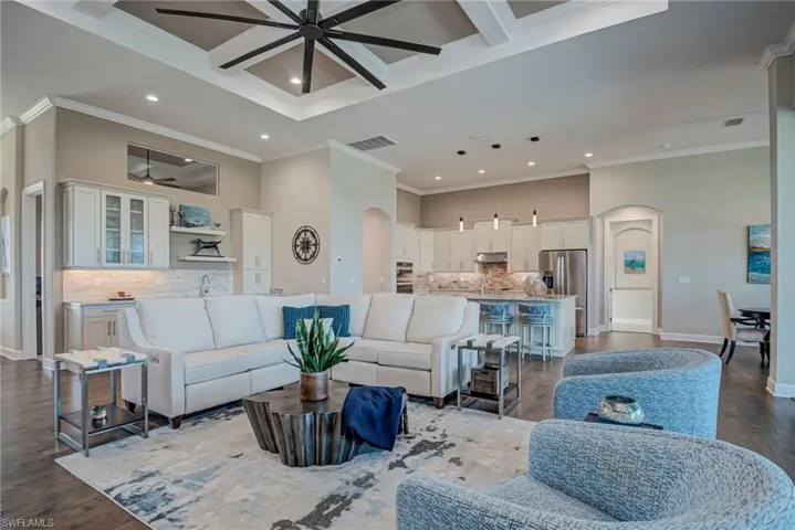 Living room with arched walkways, beam ceiling, dark wood finished floors, coffered ceiling, and ceiling fan