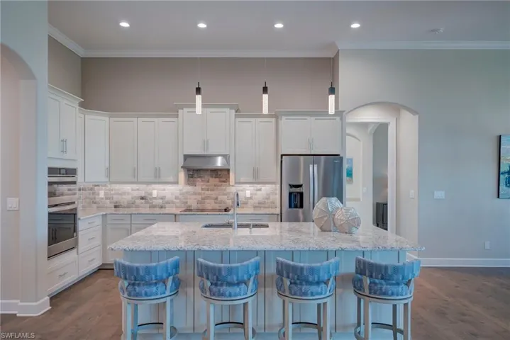 Kitchen featuring arched walkways, white cabinetry, appliances with stainless steel finishes, a breakfast bar, and crown molding