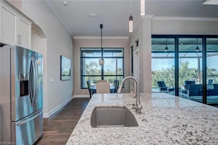 Kitchen featuring stainless steel fridge with ice dispenser, ornamental molding, pendant lighting, dark wood-style floors, and light stone countertops