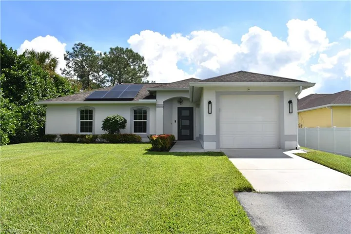 Ranch-style house with a garage, solar panels, and a front yard