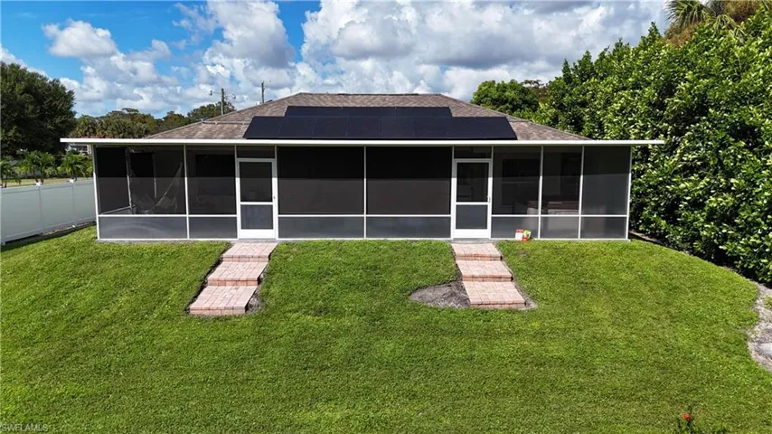 Back of house featuring a yard, solar panels, and a sunroom