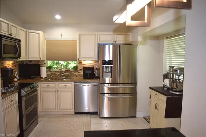 Kitchen with sink, decorative backsplash, appliances with stainless steel finishes, light tile patterned floors, and dark stone countertops