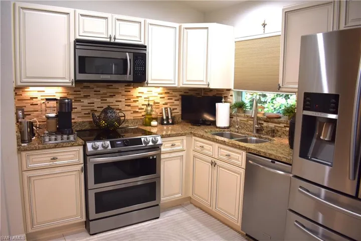 Kitchen with sink, decorative backsplash, appliances with stainless steel finishes, light tile patterned floors, and dark stone countertops