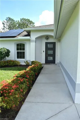 View of exterior entry with solar panels and a lawn