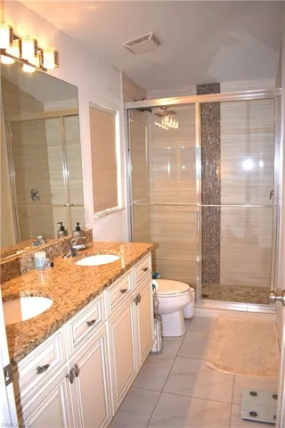 Bathroom featuring tile patterned floors, a shower with door, vanity, and toilet