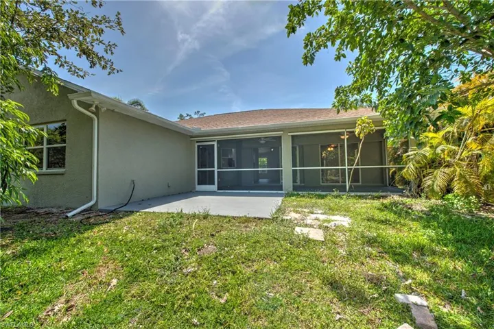 Rear view of house with stucco siding, a yard, a patio, and a sunroom