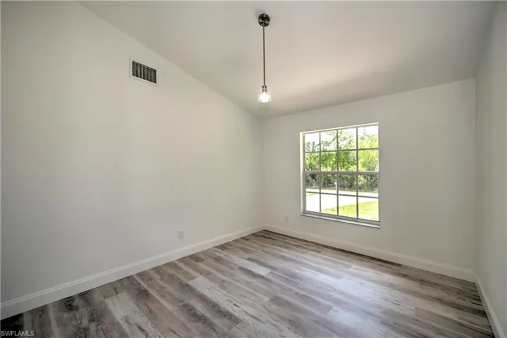 Unfurnished room with lofted ceiling, visible vents, wood finished floors, and baseboards