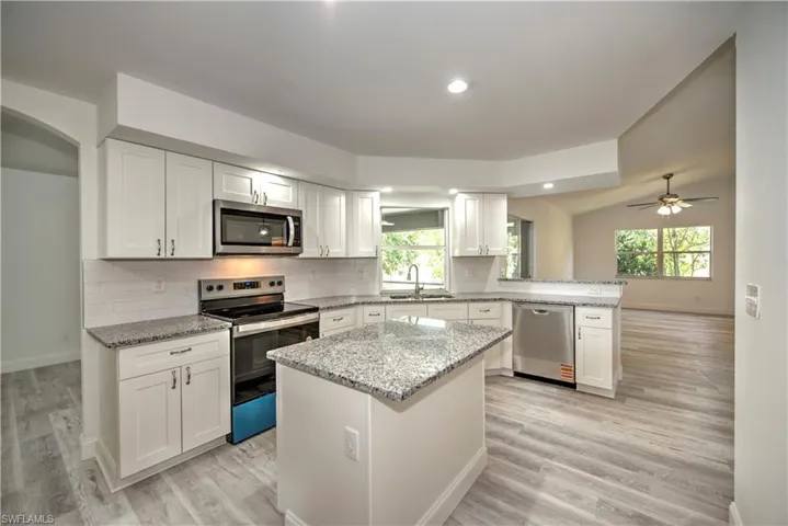 Kitchen featuring a sink, stainless steel appliances, a peninsula, baseboards, and white cabinets