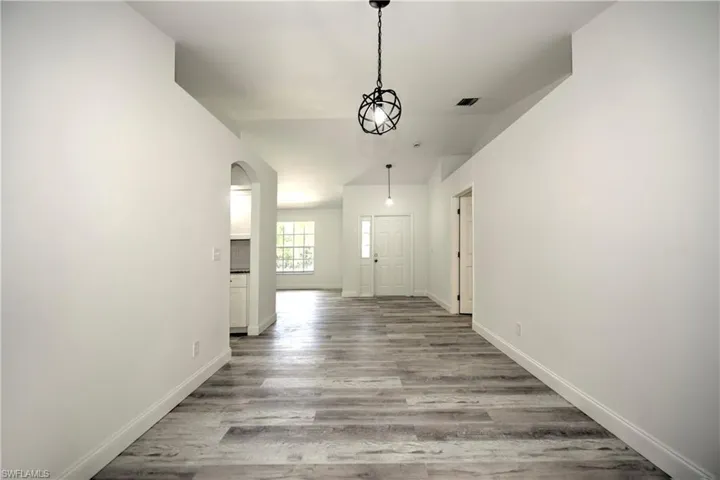 Unfurnished dining area with visible vents, baseboards, arched walkways, vaulted ceiling, and wood finished floors