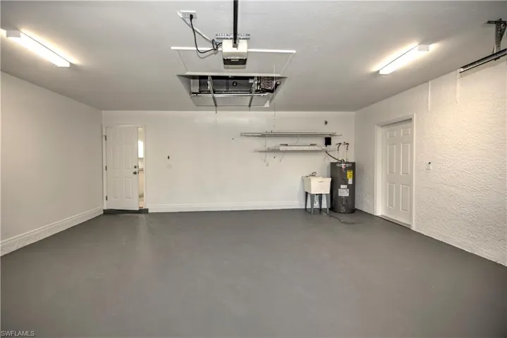 Garage with a garage door opener, a sink, electric water heater, and a textured wall