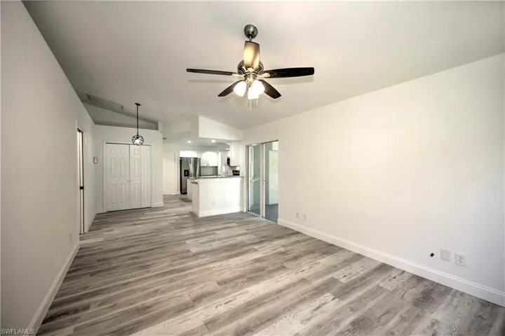 Unfurnished living room with a ceiling fan, vaulted ceiling, wood finished floors, and baseboards