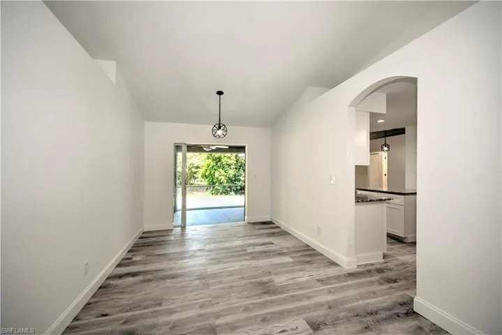 Unfurnished dining area with baseboards, arched walkways, light wood-style floors, and vaulted ceiling