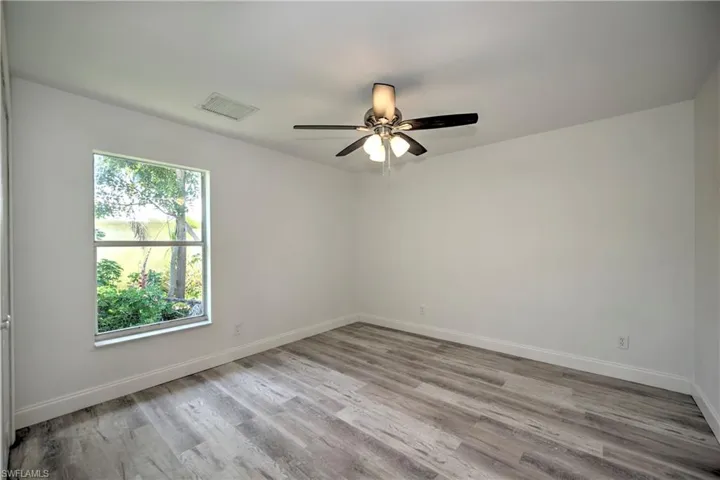 Unfurnished room with a ceiling fan, visible vents, wood finished floors, and baseboards