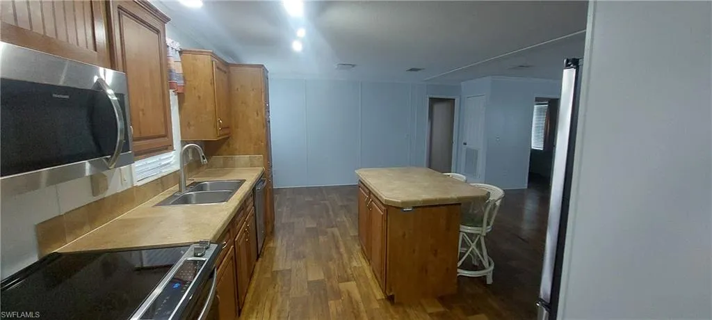 Kitchen featuring stainless steel appliances, dark wood-style flooring, a kitchen island, and light countertops